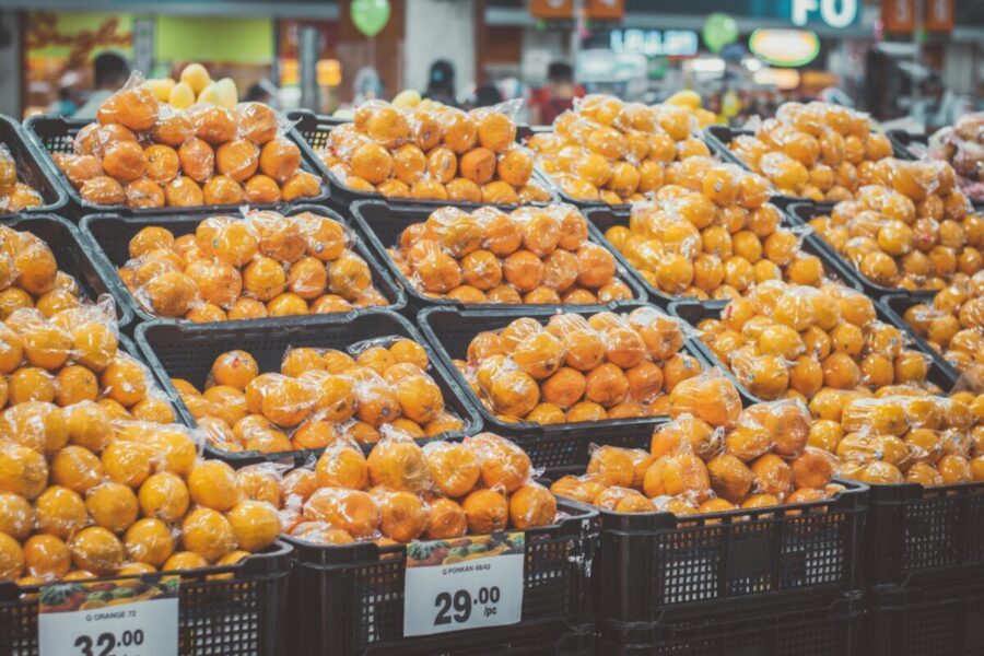 Stack of fresh oranges wrapped in plastic at a grocery store, priced with tags.