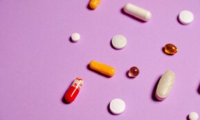 A vibrant flat lay of various pills and capsules on a purple surface.