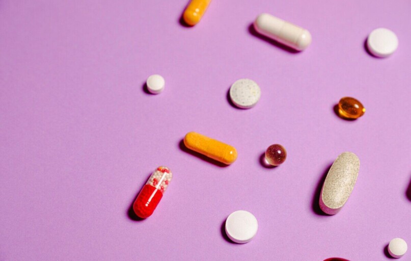 A vibrant flat lay of various pills and capsules on a purple surface.