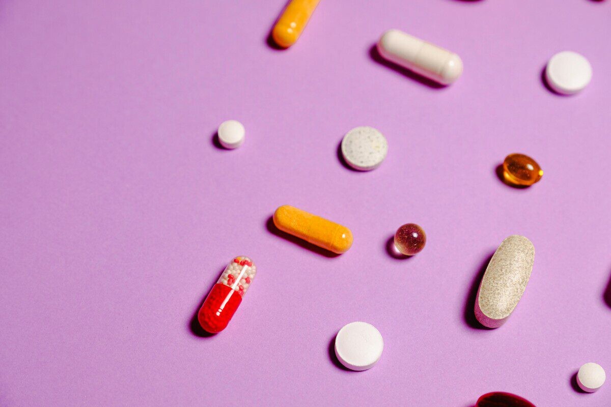 A vibrant flat lay of various pills and capsules on a purple surface.