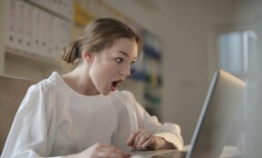 Surprised woman sitting at desk with laptop indoors, expressing amazement.