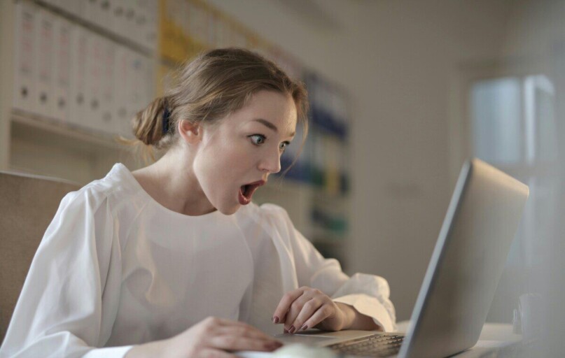 Surprised woman sitting at desk with laptop indoors, expressing amazement.