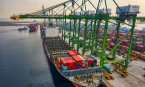 Aerial view of a cargo ship docked at New Priok Container Terminal, Jakarta, showcasing vibrant logistics activity.
