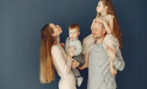 Portrait of a joyful family with parents and kids showing love and affection against a blue background.