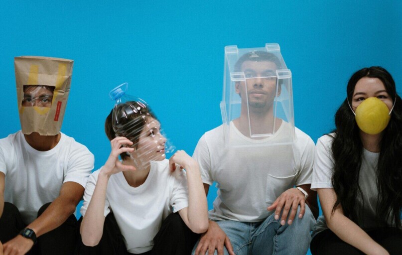 Four people wearing humorous DIY face masks against a blue background, showcasing creativity and humor.