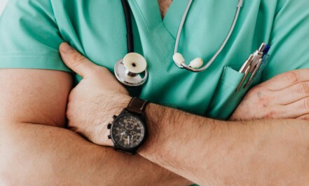Close-up of a healthcare professional with arms crossed wearing medical scrubs and stethoscope.