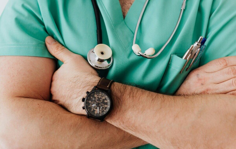 Close-up of a healthcare professional with arms crossed wearing medical scrubs and stethoscope.