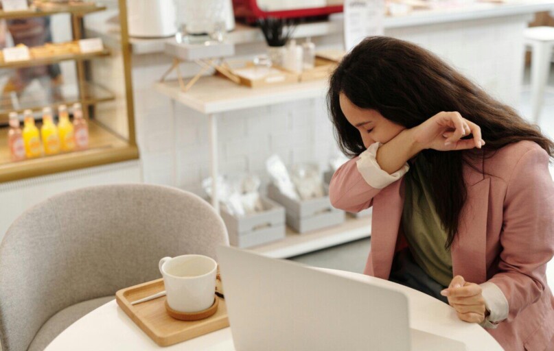 Woman covering a sneeze in a modern cafe, capturing everyday health concerns.
