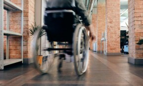 Blurred motion of a person in a wheelchair moving quickly through an indoor office hallway.