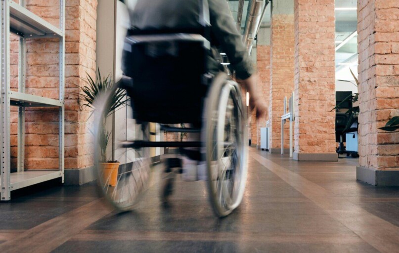 Blurred motion of a person in a wheelchair moving quickly through an indoor office hallway.