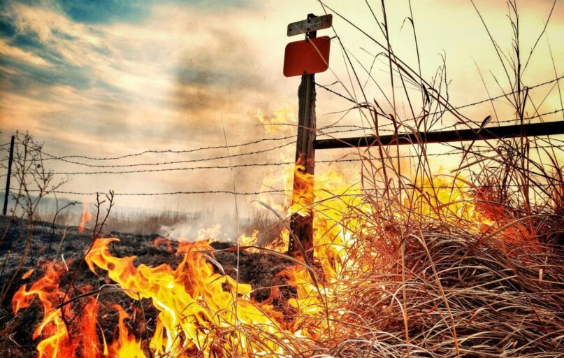 Dramatic image of a grass fire blazing near a barbed wire fence in a rural Kansas field.