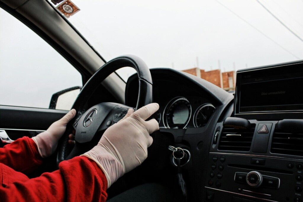 A person wearing protective gloves while driving a Mercedes-Benz, focusing on safety and hygiene.