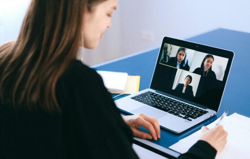 A woman engaging in a video conference using a laptop at home, taking notes.