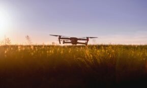 A drone flies over a field during sunset, capturing stunning aerial views.