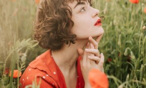 Contemplative woman in a poppy field, wearing a red polka dot dress, surrounded by vibrant flowers.