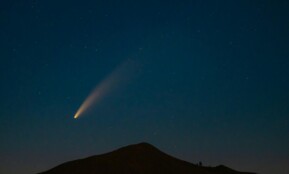 A breathtaking capture of a comet streaking across a star-filled night sky above a mountain silhouette.