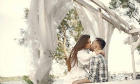 A romantic couple kissing under a white canopy in a serene outdoor setting.