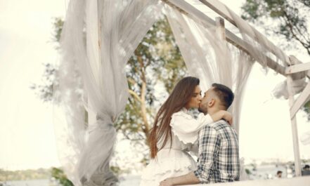 A romantic couple kissing under a white canopy in a serene outdoor setting.