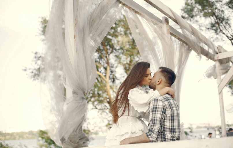 A romantic couple kissing under a white canopy in a serene outdoor setting.