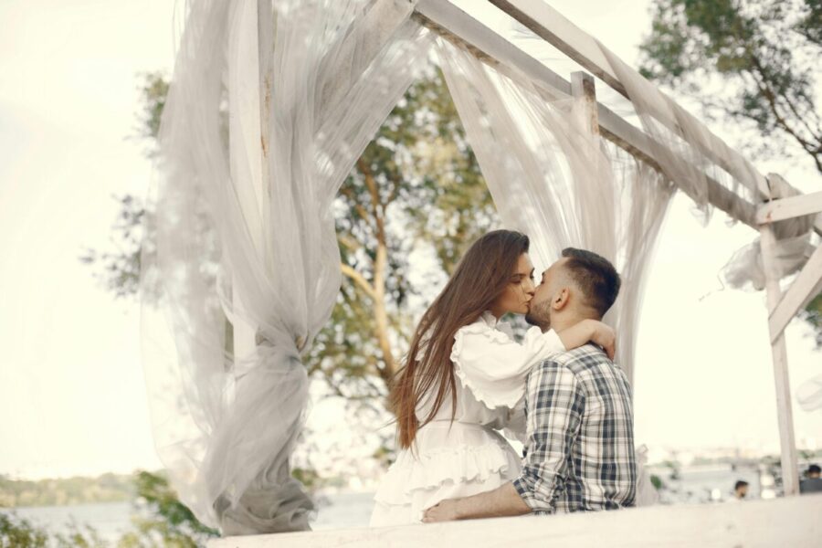 A romantic couple kissing under a white canopy in a serene outdoor setting.