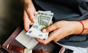 Close-up of hands counting euro notes above a wristwatch in a box.
