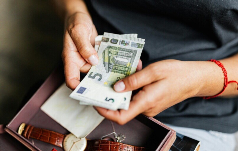Close-up of hands counting euro notes above a wristwatch in a box.