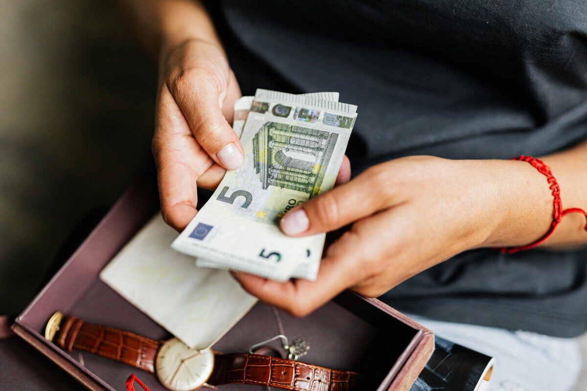 Close-up of hands counting euro notes above a wristwatch in a box.
