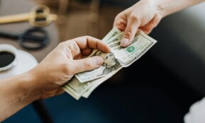 A close-up image of hands exchanging US dollar bills, symbolizing financial transaction or payment.
