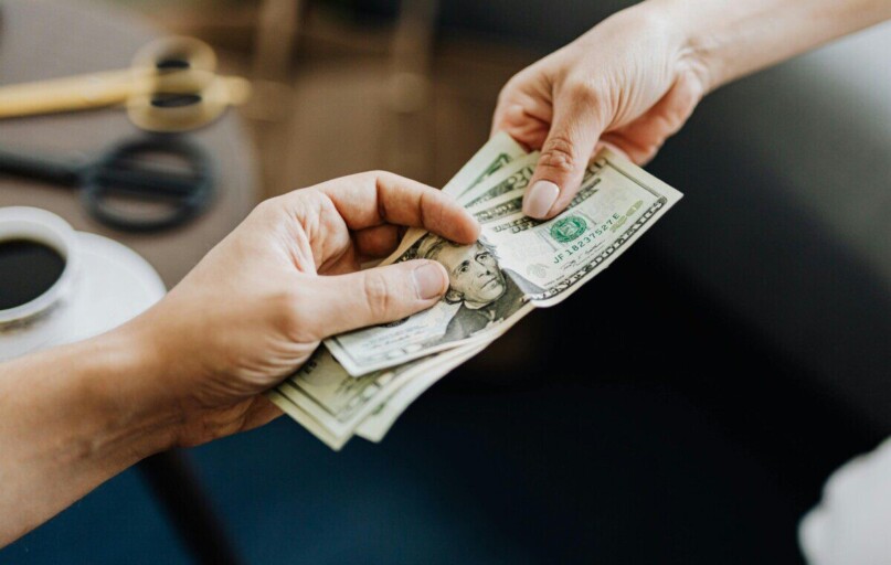 A close-up image of hands exchanging US dollar bills, symbolizing financial transaction or payment.