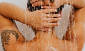 A woman with a tattoo enjoys a refreshing shower, symbolizing cleanliness and relaxation.