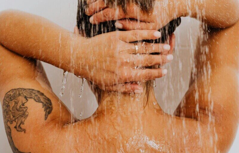 A woman with a tattoo enjoys a refreshing shower, symbolizing cleanliness and relaxation.