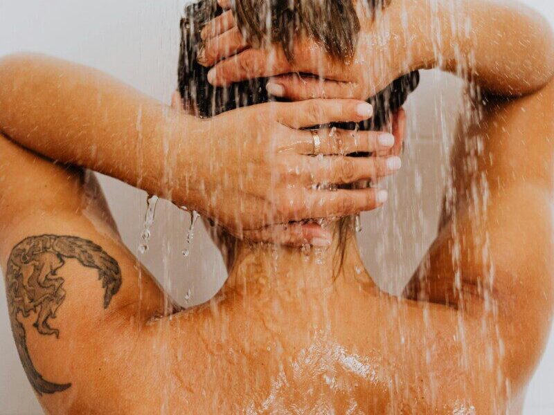 A woman with a tattoo enjoys a refreshing shower, symbolizing cleanliness and relaxation.