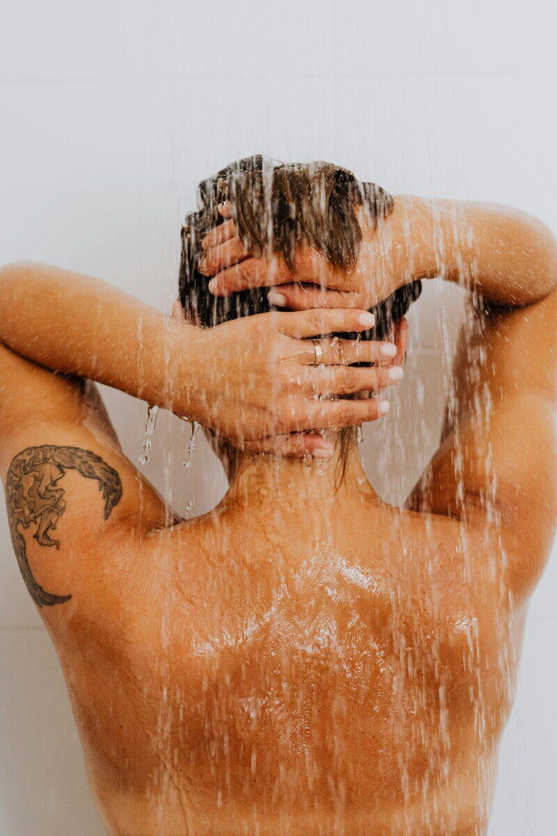 A woman with a tattoo enjoys a refreshing shower, symbolizing cleanliness and relaxation.