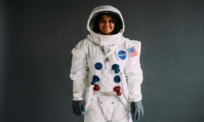 Portrait of a woman in a NASA astronaut costume, smiling against a neutral background.
