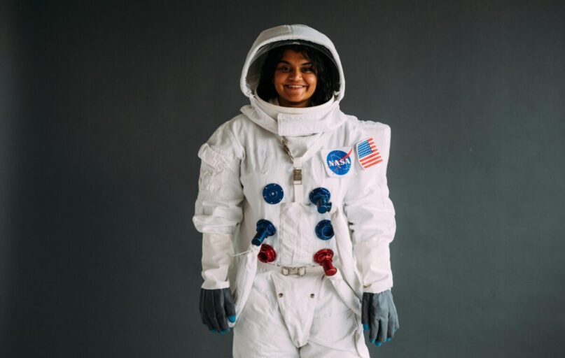 Portrait of a woman in a NASA astronaut costume, smiling against a neutral background.