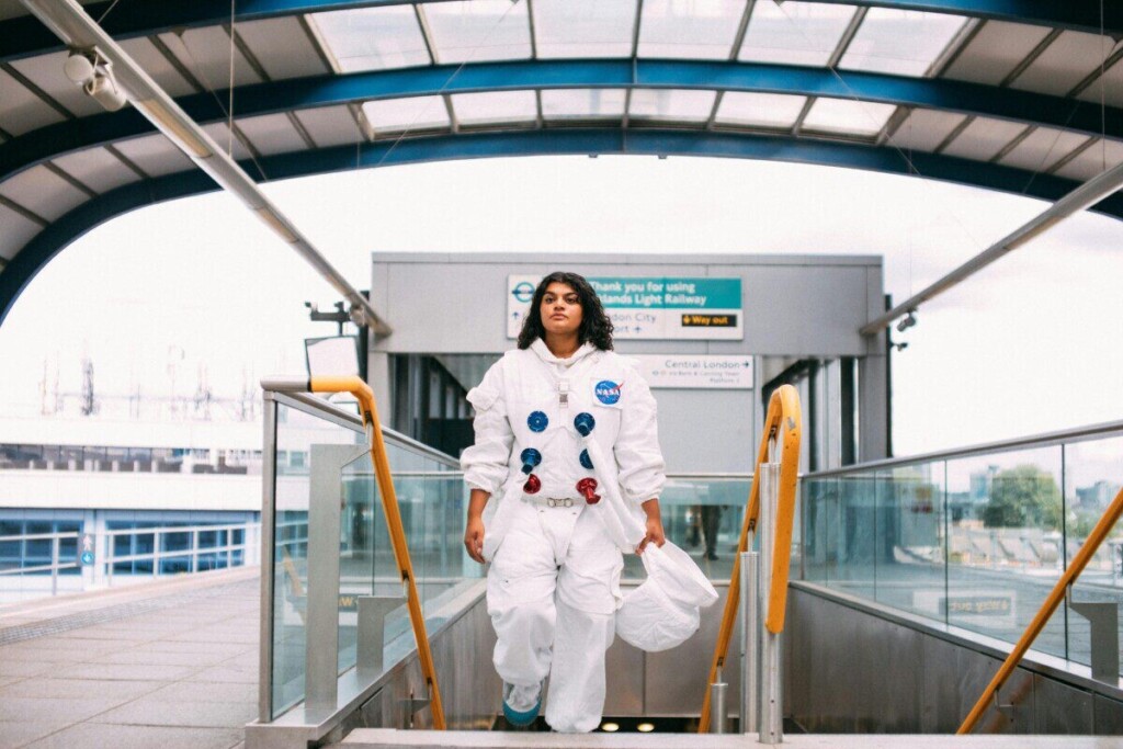 Individual in an astronaut suit walking at a modern railway platform.