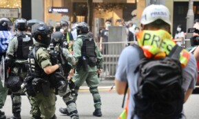 Riot police and journalists during a city protest, wearing protective gear.