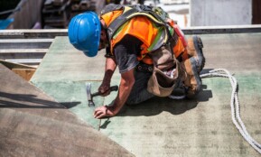 A skilled construction worker in protective gear hammering a rooftop panel.