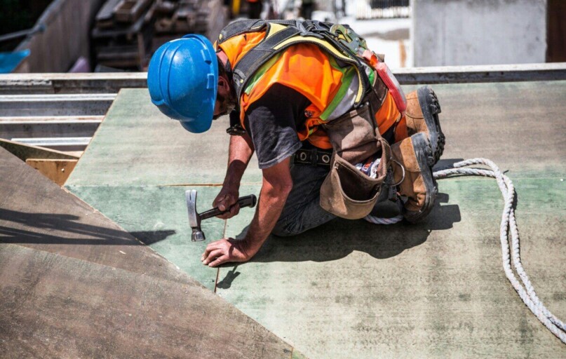 A skilled construction worker in protective gear hammering a rooftop panel.