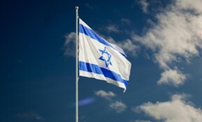 The Israeli national flag waving against a clear blue sky with clouds.