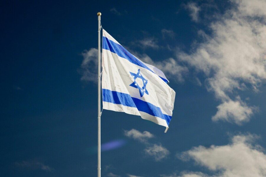 The Israeli national flag waving against a clear blue sky with clouds.