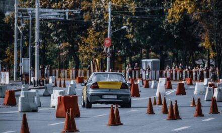 Participant in car race maneuvering between red and white traffic cones or barriers in front of audience