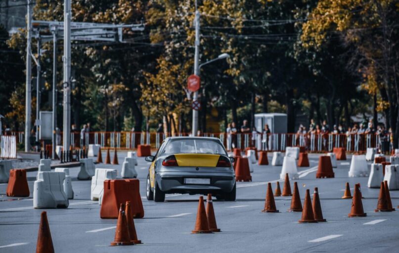 Participant in car race maneuvering between red and white traffic cones or barriers in front of audience