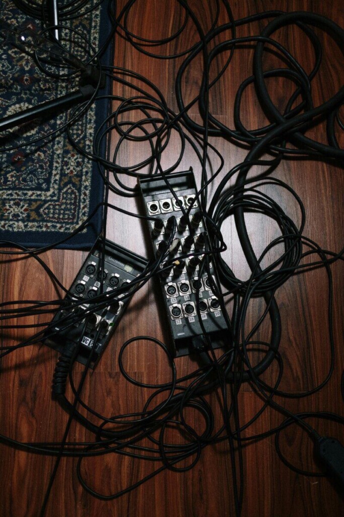 Overhead view of tangled audio cables and equipment on a wooden floor in a studio setting.