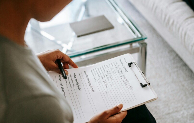 From above of blurred anonymous female psychologist reading documents on clipboard while sitting in office near table during session