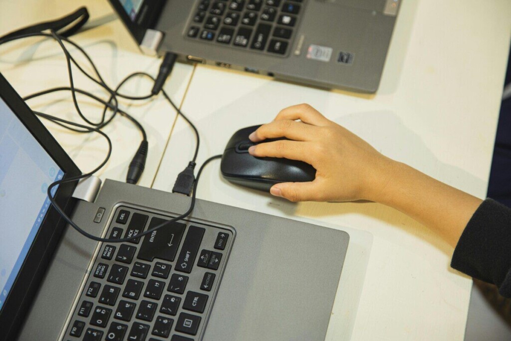 A child's hand on a mouse by a laptop in an educational setting, high angle.