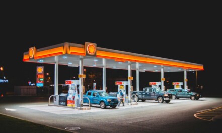 A glowing Shell gas station at night with parked vehicles and vibrant lighting.