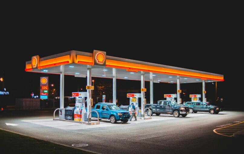 A glowing Shell gas station at night with parked vehicles and vibrant lighting.