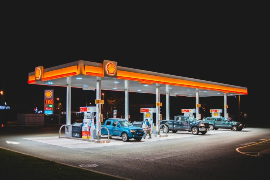 A glowing Shell gas station at night with parked vehicles and vibrant lighting.