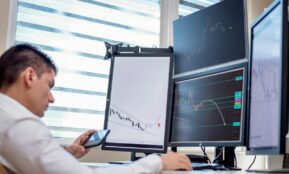 A stock trader analyzes financial data on multiple computer screens in an office setting.
